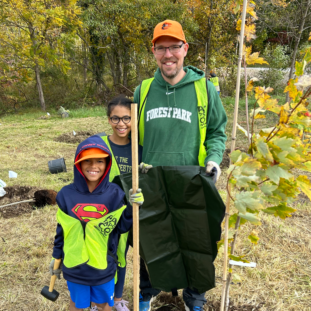 A family of three volunteers stand near a newly planted tree at Serenity Ridge Natural Burial Cemetery and Arboretum in Windsor Mill, Maryland.