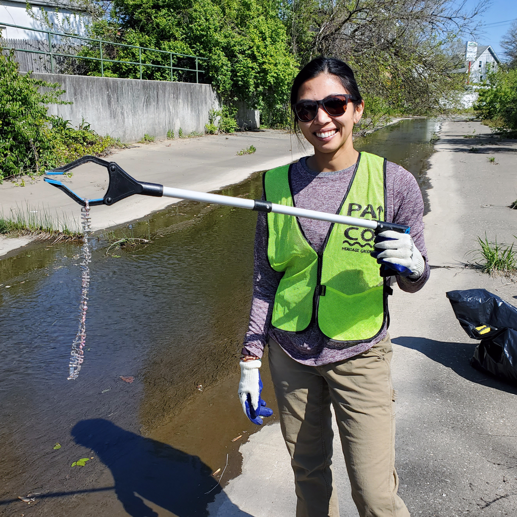 A volunteer holds a trash pickup tool with trash grabbed from the water at an environmental cleanup event.