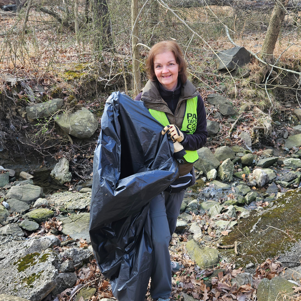 A volunteer near a stream holds up a trash bag during a Stream Cleanup stewardship event.